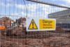 A construction site fenced of with "danger demolition in progress" warning sign
