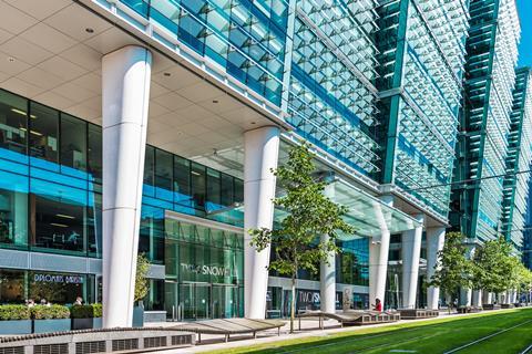 A picture of Birmingham's office in Birmingham. There is a tram route through grass in front of the glass and steel office